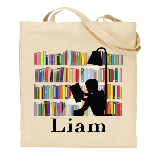 Beige tote bag with a design of a person reading a book in front of a bookshelf and the name 'Liam' on a white background.