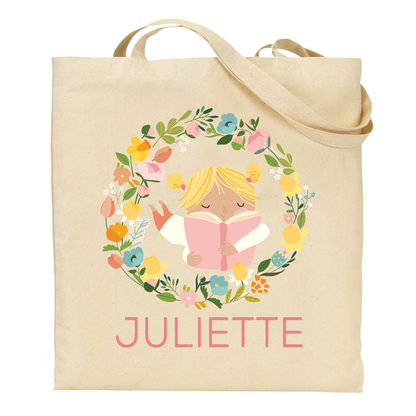 canvas tote bag with a design of a blonde girl reading a book surrounded by flowers and the name 'Juliette' on a white background.