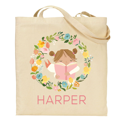 canvas tote bag with a brunette girl reading a book surrounded by flowers and the name 'Harper' on a white background.